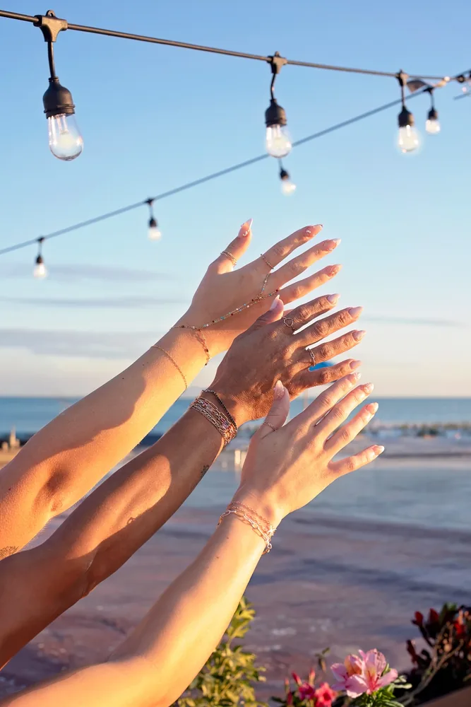 Arms reaching toward the sky wearing stacked permanent jewelry at a group event
