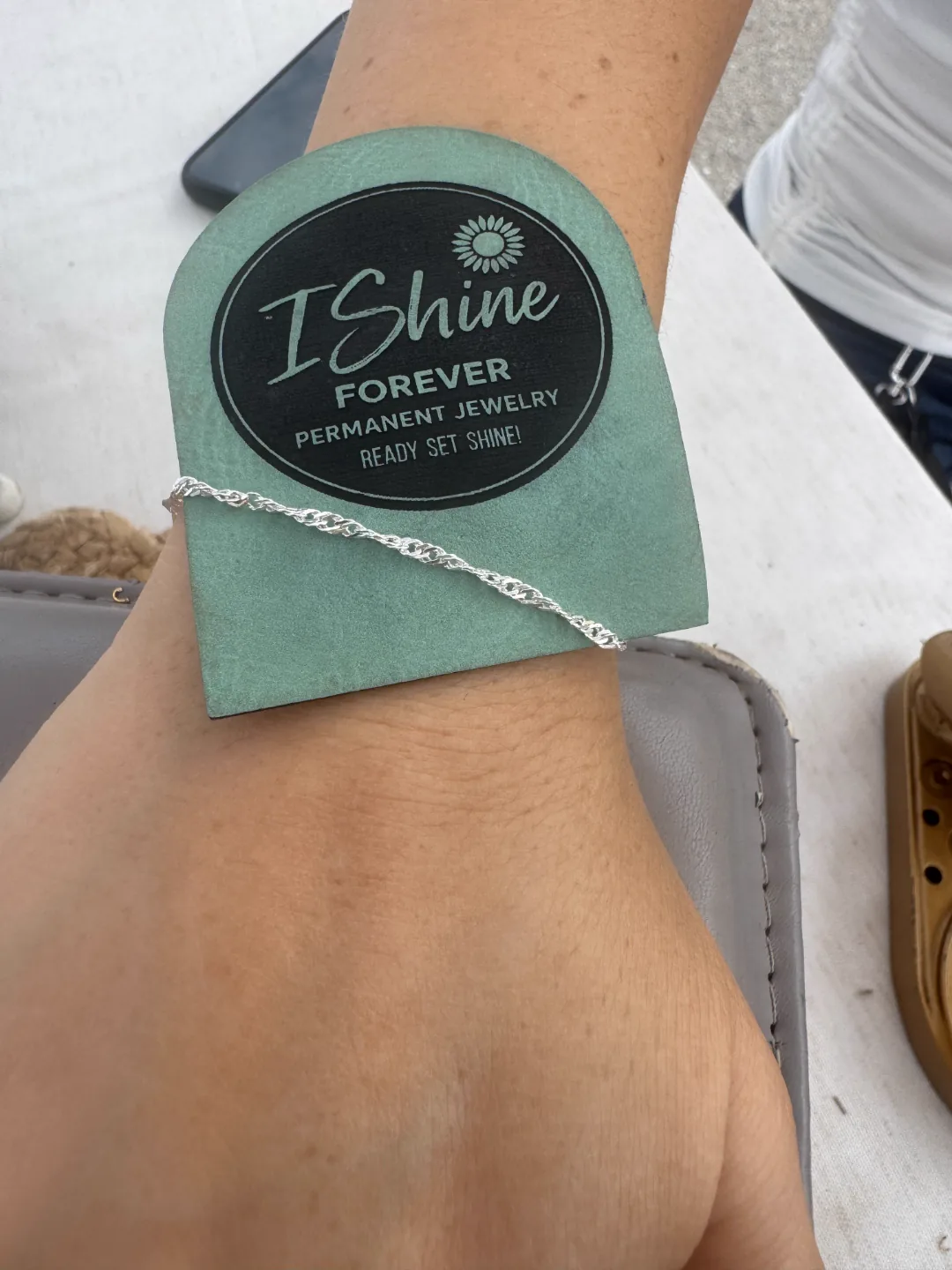 Finished silver permanent bracelet on a client's wrist with an I Shine Forever branded card