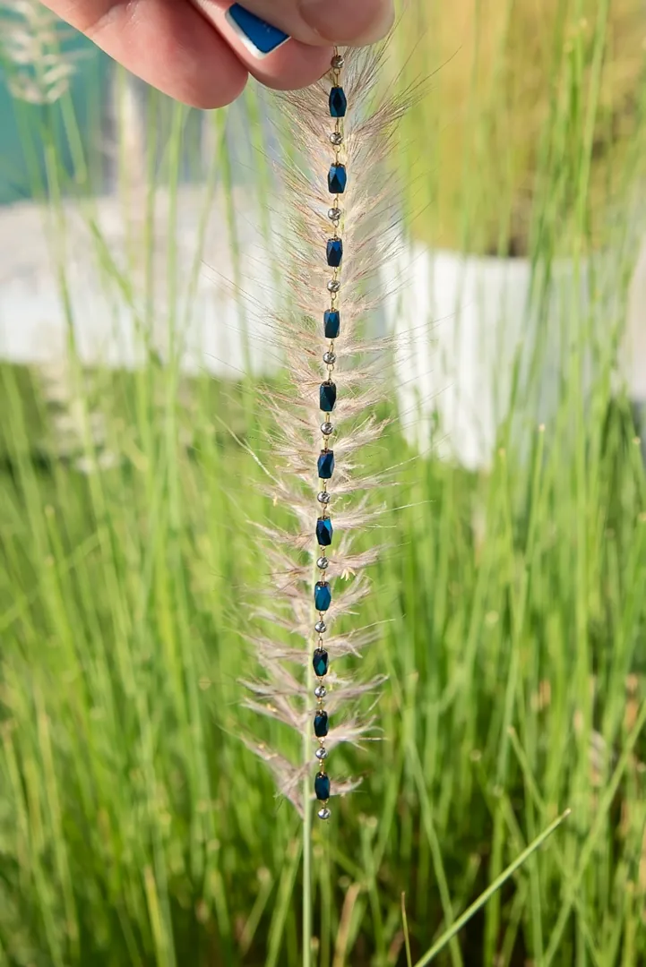 Gold chain set with deep blue faceted stones held up against beach grass at golden hour