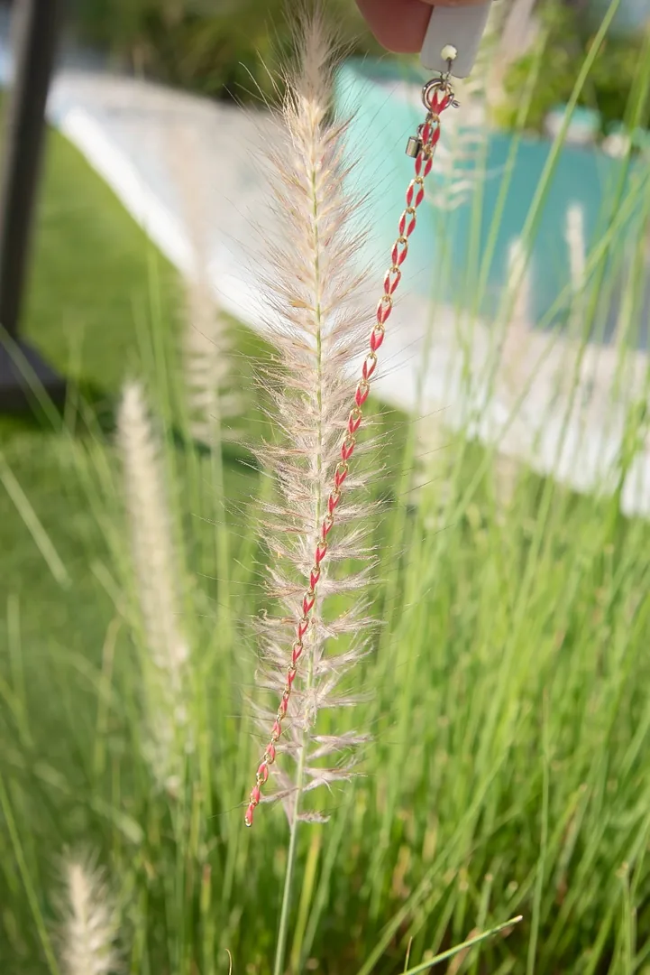 Coral red and gold infinity-link chain held against beach grass by the pool