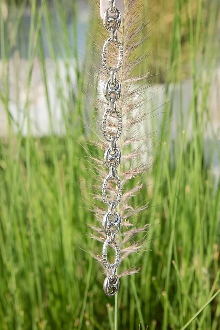 Sterling silver mariner and pavΓ© link chain held against sunlit beach grass