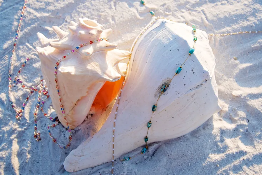 Gold chains and turquoise stones draped over conch shells on the sand