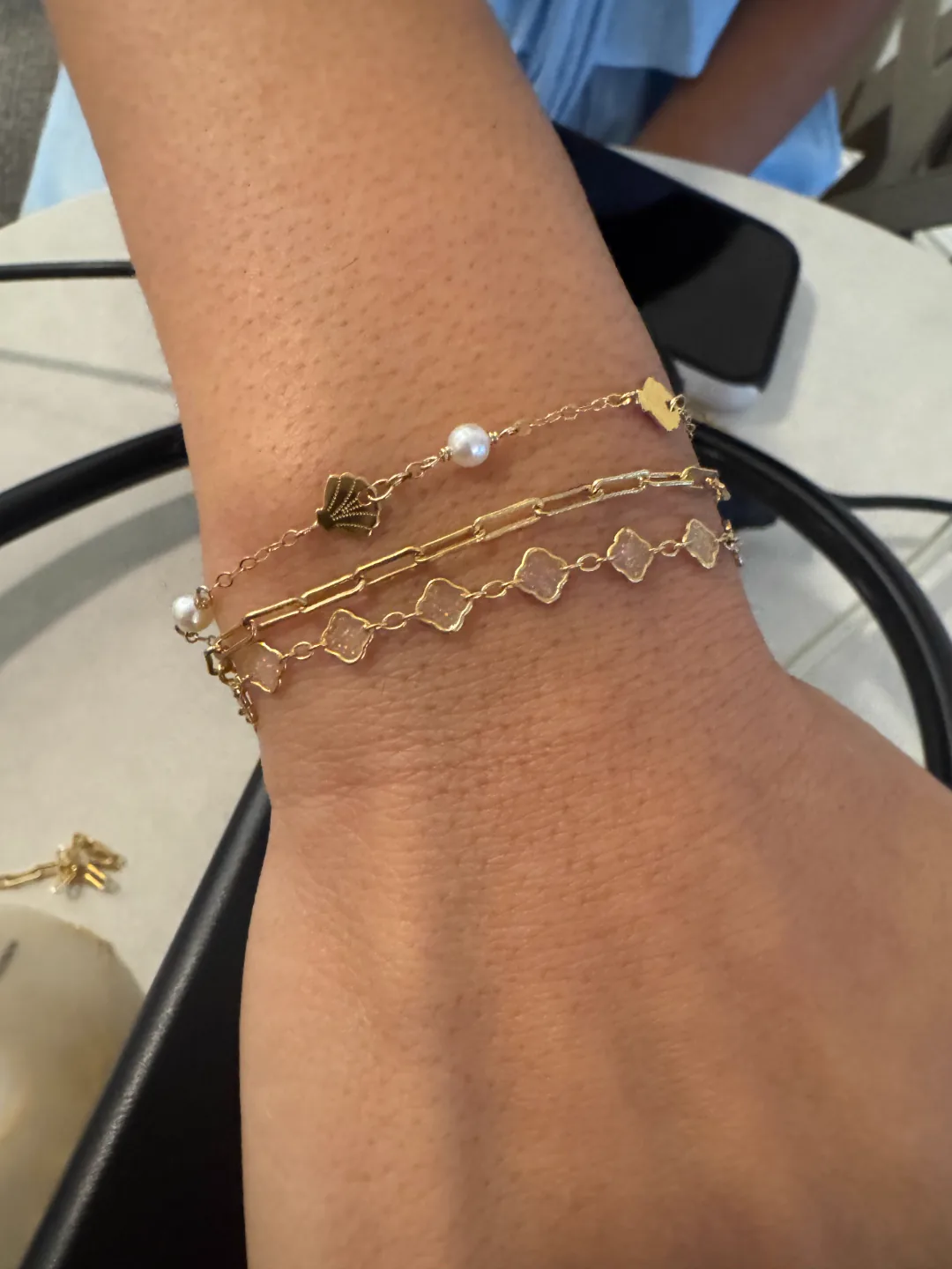 Layered gold permanent bracelet stack with pearls, shell charms and clover links