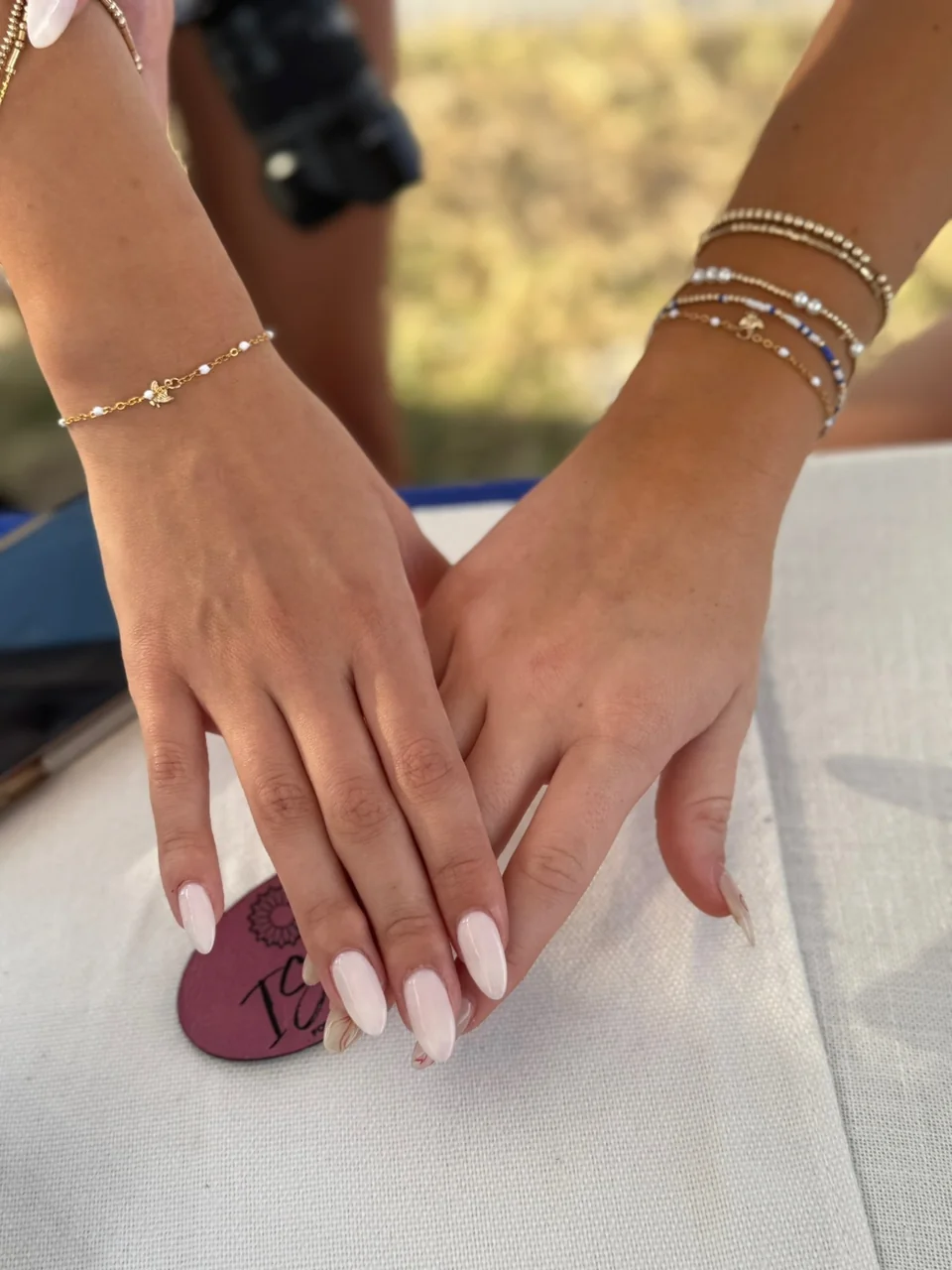 Two hands joined together showing stacked gold permanent bracelets with pearls and charms