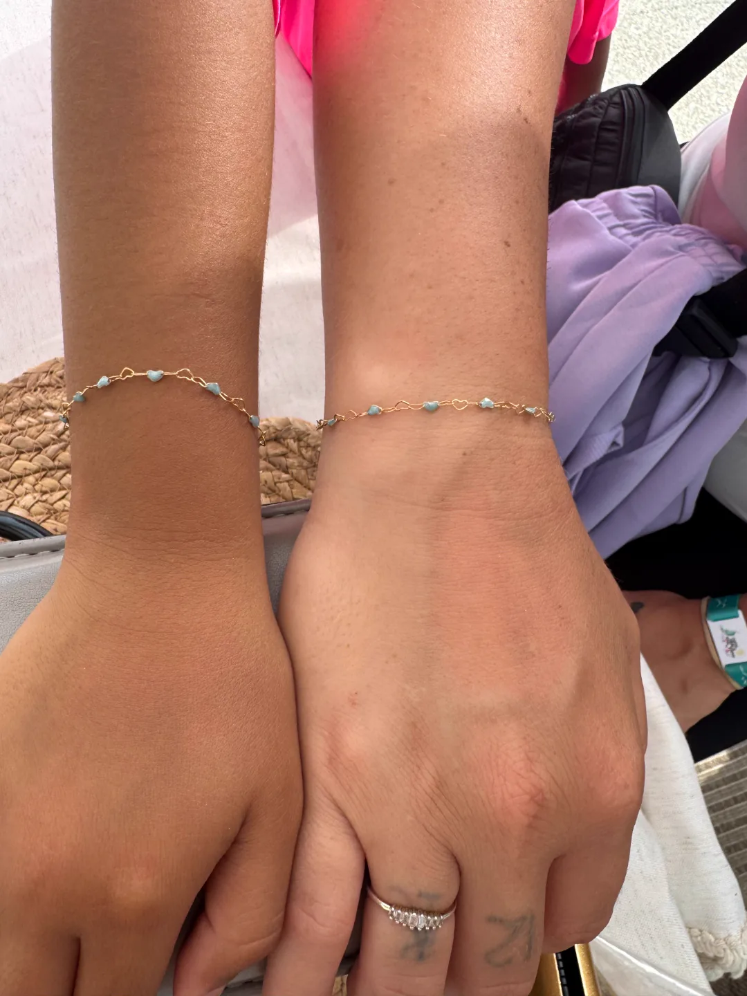 Two matching gold and pale-blue larimar heart permanent bracelets on friends' wrists