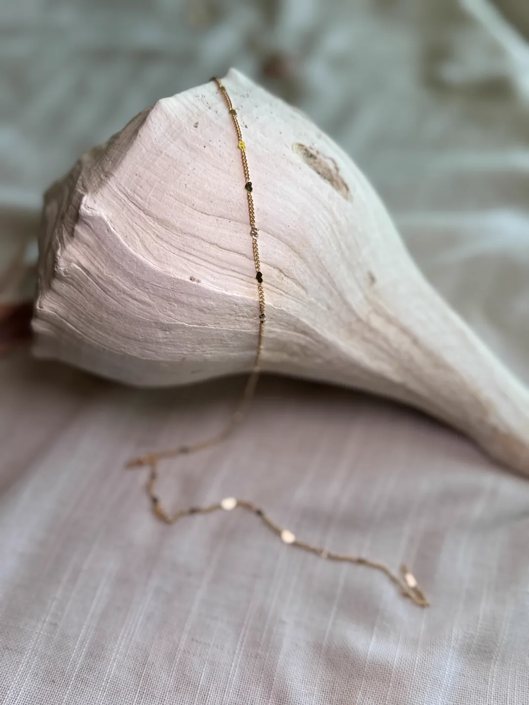 Fine gold satellite chain gently curving over a soft conch shell