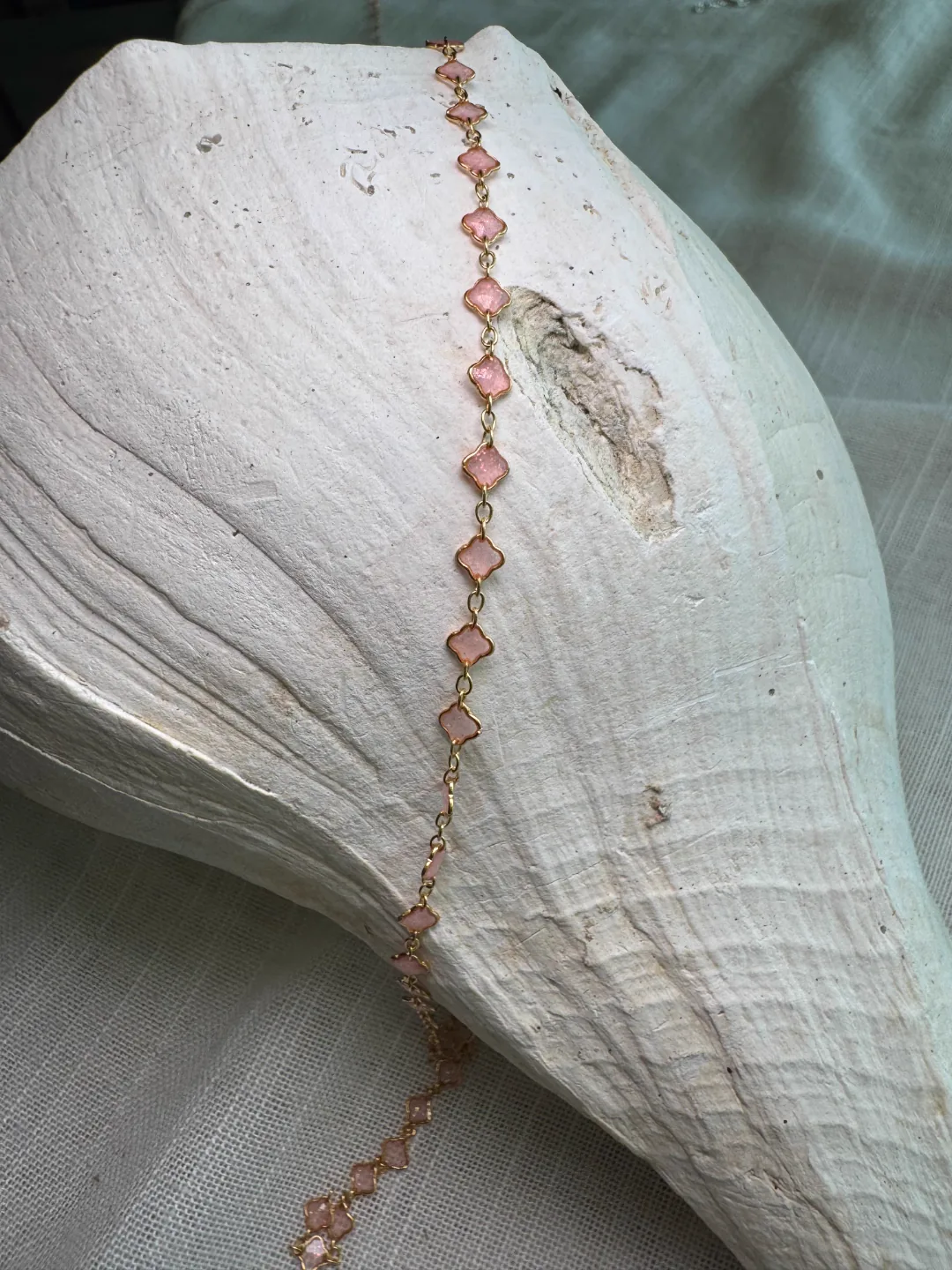 Rose-gold clover charm chain draped across a white conch shell