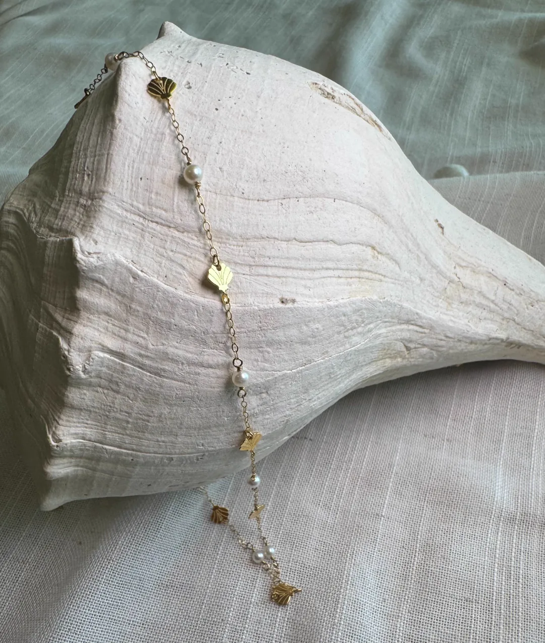 Gold chain with mini gold shell charms and freshwater pearls resting on a large conch