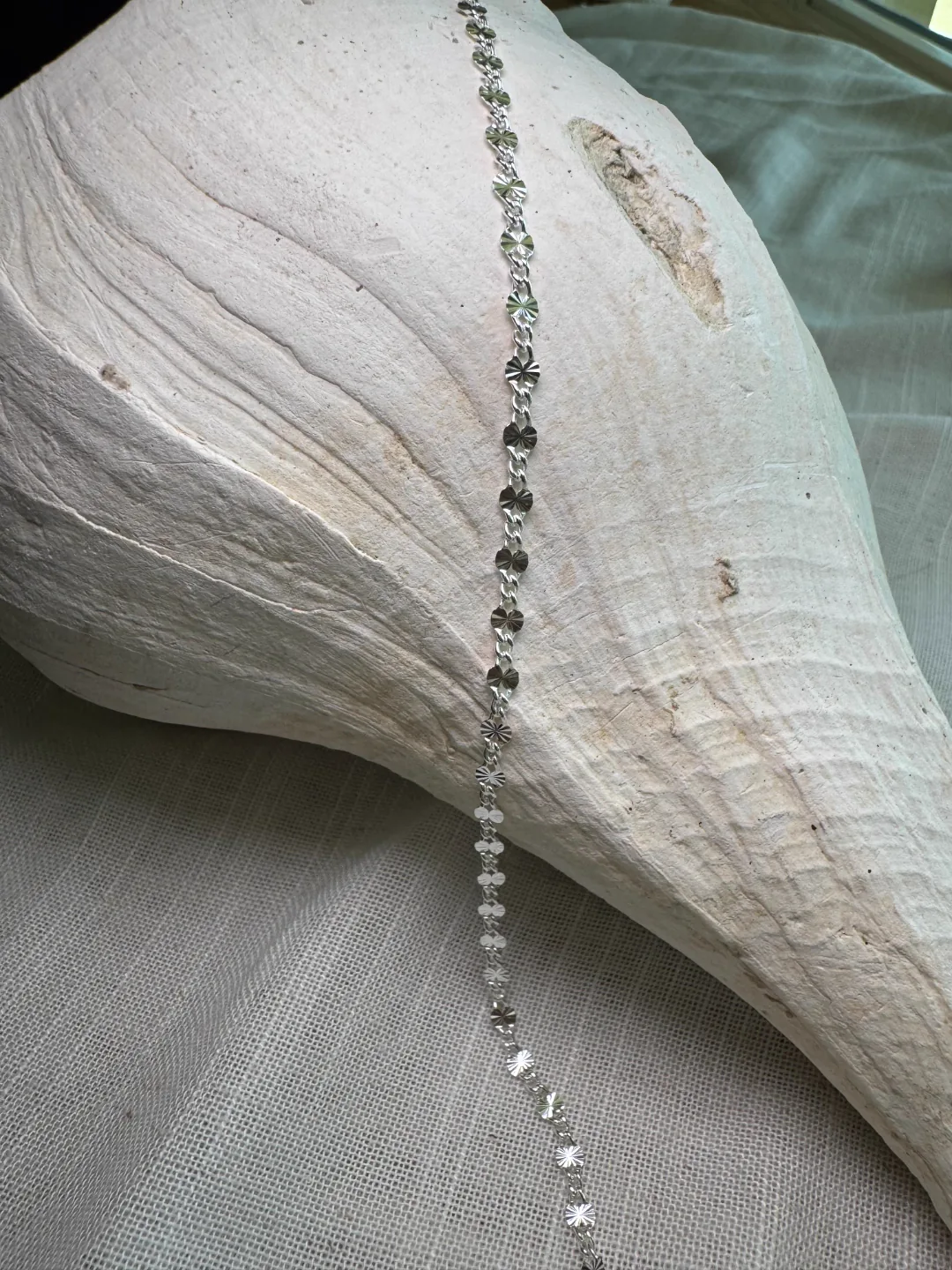 Delicate silver flower-link permanent chain resting on a white conch shell