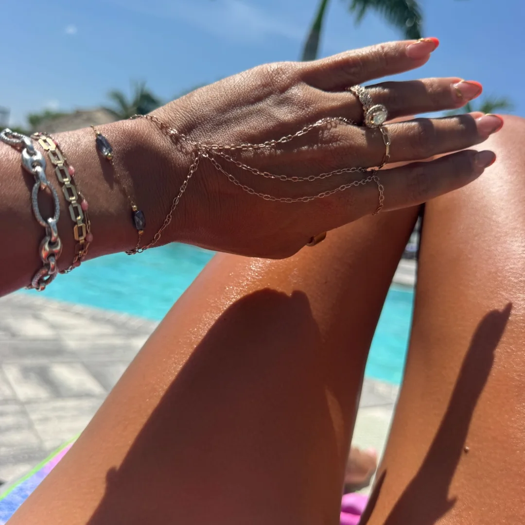Gold hand chain, bracelets and rings shown over a swimming pool