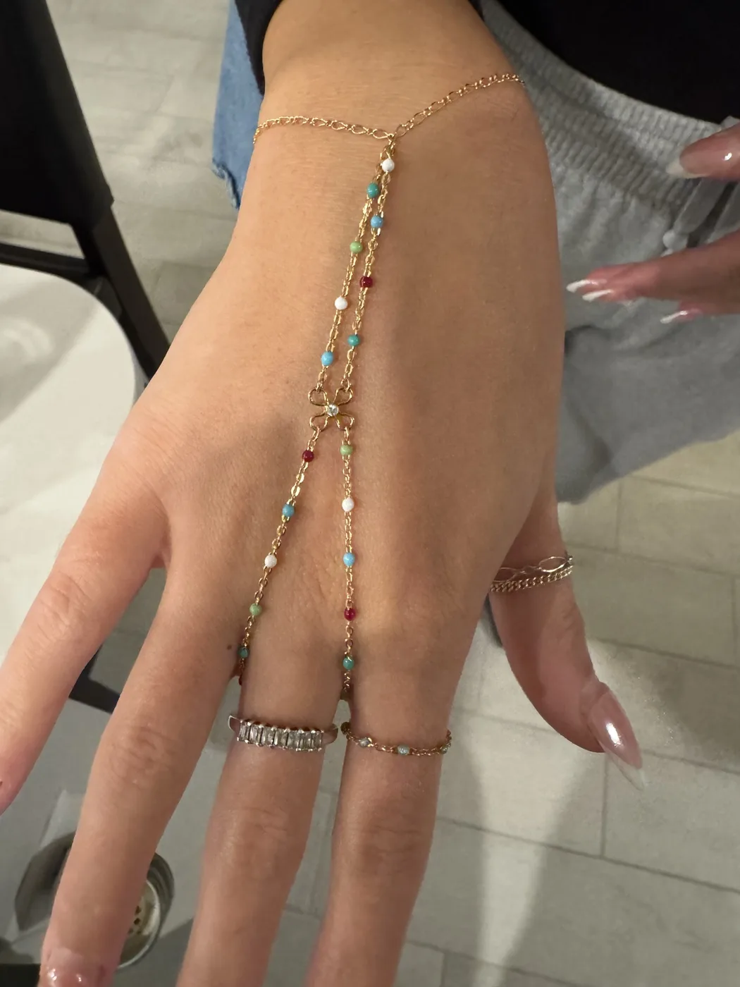 Colorful beaded gold hand chain with a clover charm connecting to two rings